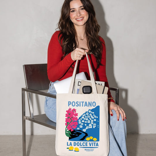Woman holding a tote bag with 'Positano La Dolce Vita' design.