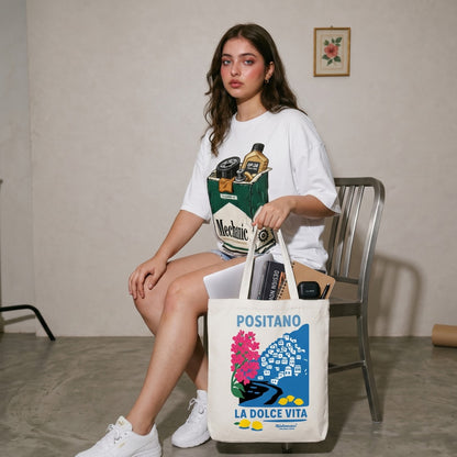 Woman holding a tote bag with 'Positano La Dolce Vita' design, sitting on a chair.