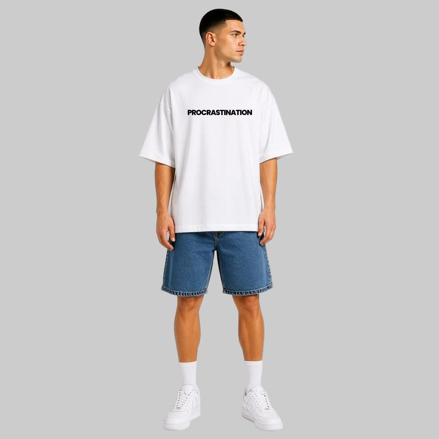 Person wearing a white t-shirt with 'PROCRASTINATION' text and blue shorts on a light gray background