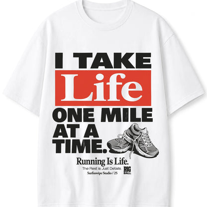 A white short-sleeve graphic T-shirt featuring a bold typographic design in black and red with the phrase 'I TAKE Life ONE MILE AT A TIME.' A grayscale running shoe illustration appears near the lower right of the print.