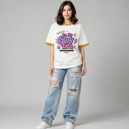 A woman modeling a white graphic t-shirt with yellow trim and distressed light blue jeans, standing against a neutral gray studio background.