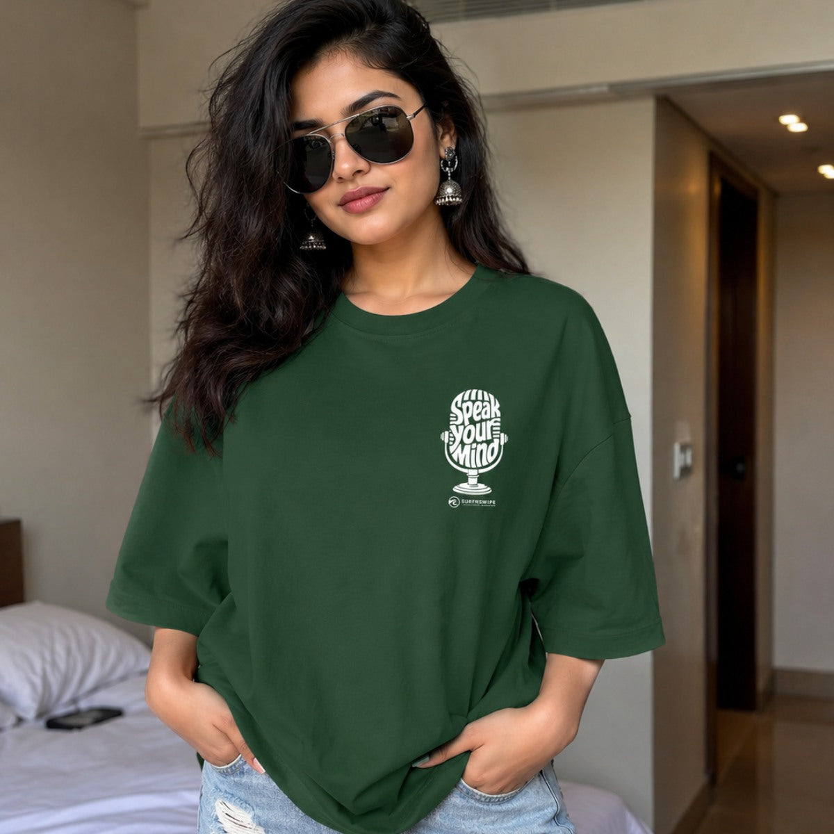 Woman wearing a green t-shirt with a logo and text in a bedroom setting