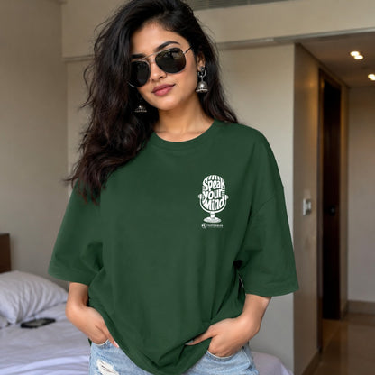 Woman wearing a green t-shirt with a logo and text in a bedroom setting