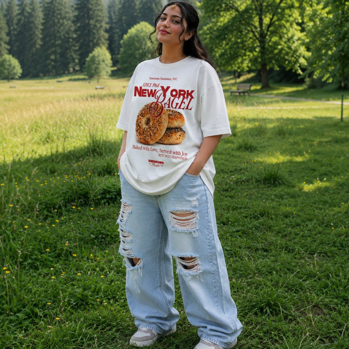 Person wearing a New York Bagel t-shirt and ripped jeans standing in a grassy field.