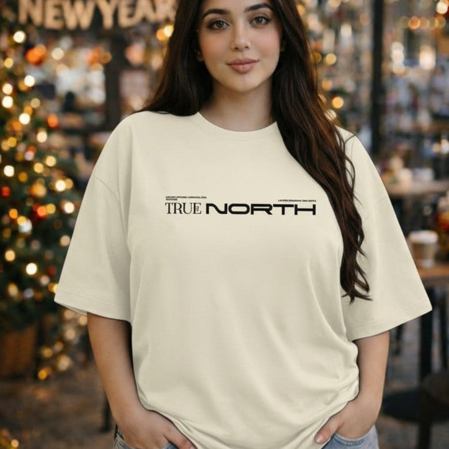 Person wearing a beige t-shirt with 'TRUE NORTH' text in a festive indoor setting.