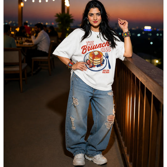 Woman wearing a 'The Brunch Club' t-shirt on a rooftop at dusk.