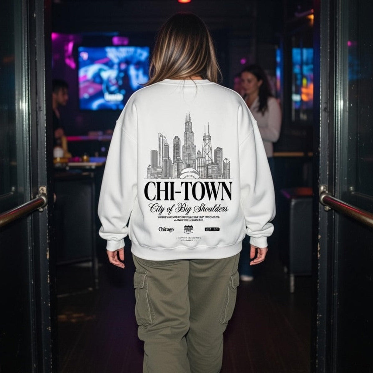 Person wearing a sweatshirt with 'CHI-TOWN City of Big Shoulders' design in a bar setting.