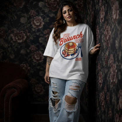 Woman wearing a 'The Brunch Club' t-shirt with a graphic design against a floral-patterned wall.