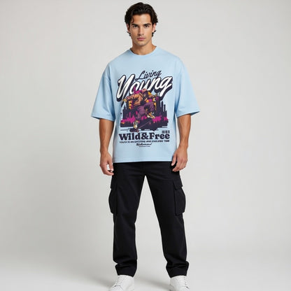 Man wearing a light blue graphic t-shirt with text and graphics, standing against a plain background