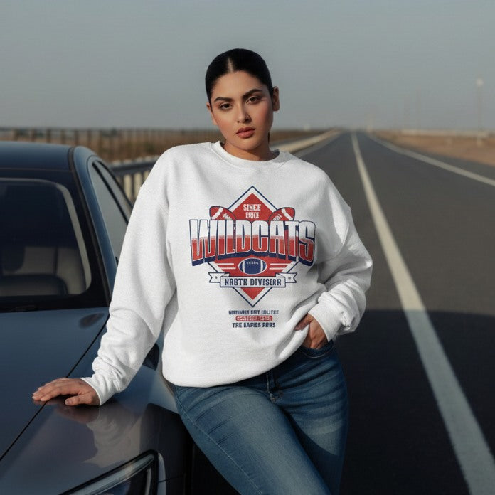 Woman wearing a white sweatshirt with a graphic design, sitting on a car by a road.