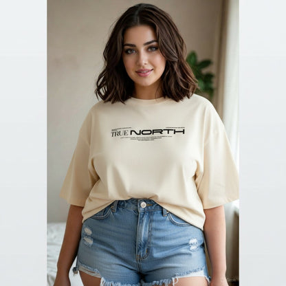 Woman wearing a beige 'True North' t-shirt and denim shorts indoors.