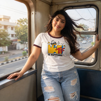A woman posing inside a train or bus, wearing a white ringer t-shirt with a colorful graphic print that reads 'MTR IS HAPPENING' and distressed light-wash jeans.