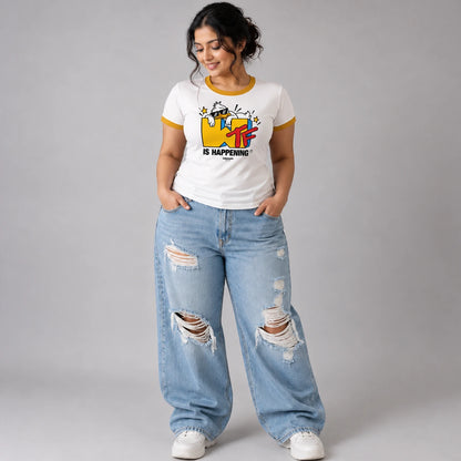 A woman modeling a white ringer t-shirt with yellow trim and a colorful MTV graphic, paired with distressed light blue jeans and white sneakers, against a neutral gray background.