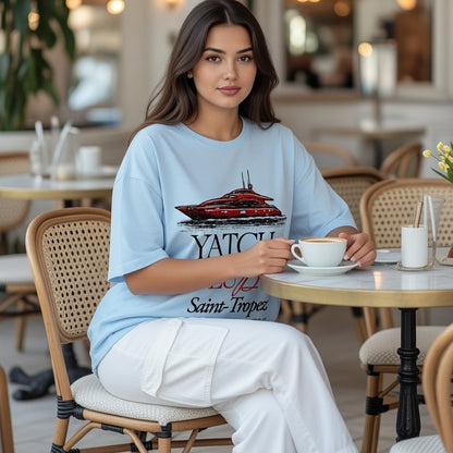 Woman sitting at a cafe table holding a cup, wearing a blue t-shirt with a graphic design.